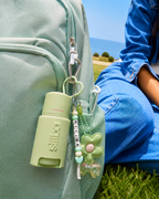 A pastel green Siiiba deodorant is clipped to a mint backpack with a personalized beaded keychain, flower charm, and playful accessories beside a tween sitting outdoors near the ocean. Designed for kids, tweens, and teens, Siiiba’s portable deodorant makes everyday body odor care easy for school, sports, travel, sleepovers, and growing-up routines. The clip-on packaging keeps a first deodorant accessible, fun, and easy to carry.