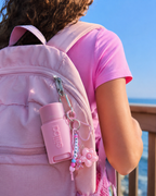 A tween wearing a pink backpack carries a pink Siiiba deodorant clipped to the outside with a personalized keychain and flower charm. Designed for kids, tweens, and teens, Siiiba’s portable deodorant makes everyday body odor care easy for school, sports, travel, and growing bodies. The fun clip-on packaging keeps a first deodorant accessible and helps young people build a simple, confident personal care routine.